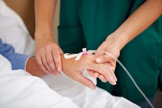 A healthcare worker gently holding a patient’s hand to check the IV catheter placed on the hand.