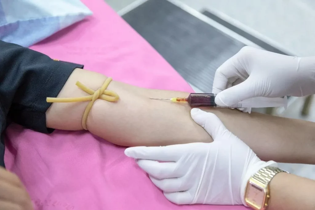Nurse performing a venipuncture to draw blood from a patient’s arm using a syringe and tourniquet for laboratory testing